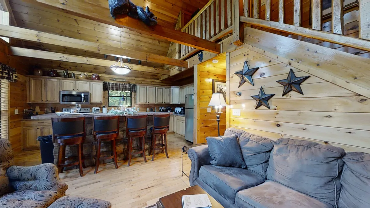The interior view features a cozy seating area with a sofa, kitchen island with bar stools, wooden beams, and playful decorative stars. The arrangement is ideal for families to socialize, dine, or unwind together, capturing the spirit of fun and togetherness.