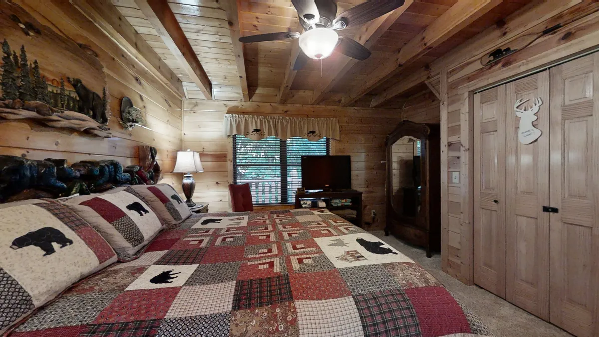A comfortable bedroom with a colorful patchwork quilt, rustic wooden decor, a window framed by curtains, and a television. The space feels homey and restful, ideal for unwinding after a day of exploration. The window connects the interior to the peaceful outdoors, suggesting a blend of comfort and nature.