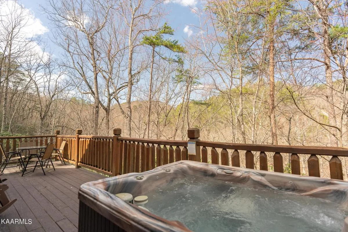 A peaceful exterior shot showcasing the wooden deck with the hot tub as a focal point, surrounded by lush foliage and trees. The natural light and open space evoke relaxation and opportunities for stargazing or enjoying quiet moments.