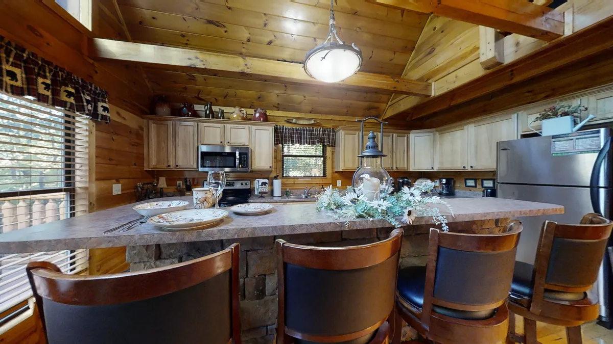 Another view of a spacious kitchen and dining area, featuring a prominent kitchen island with bar stools, wooden cabinetry, and decorative touches. The scene suggests group activities such as holiday celebrations or casual gatherings, with enough space for everyone to join in.