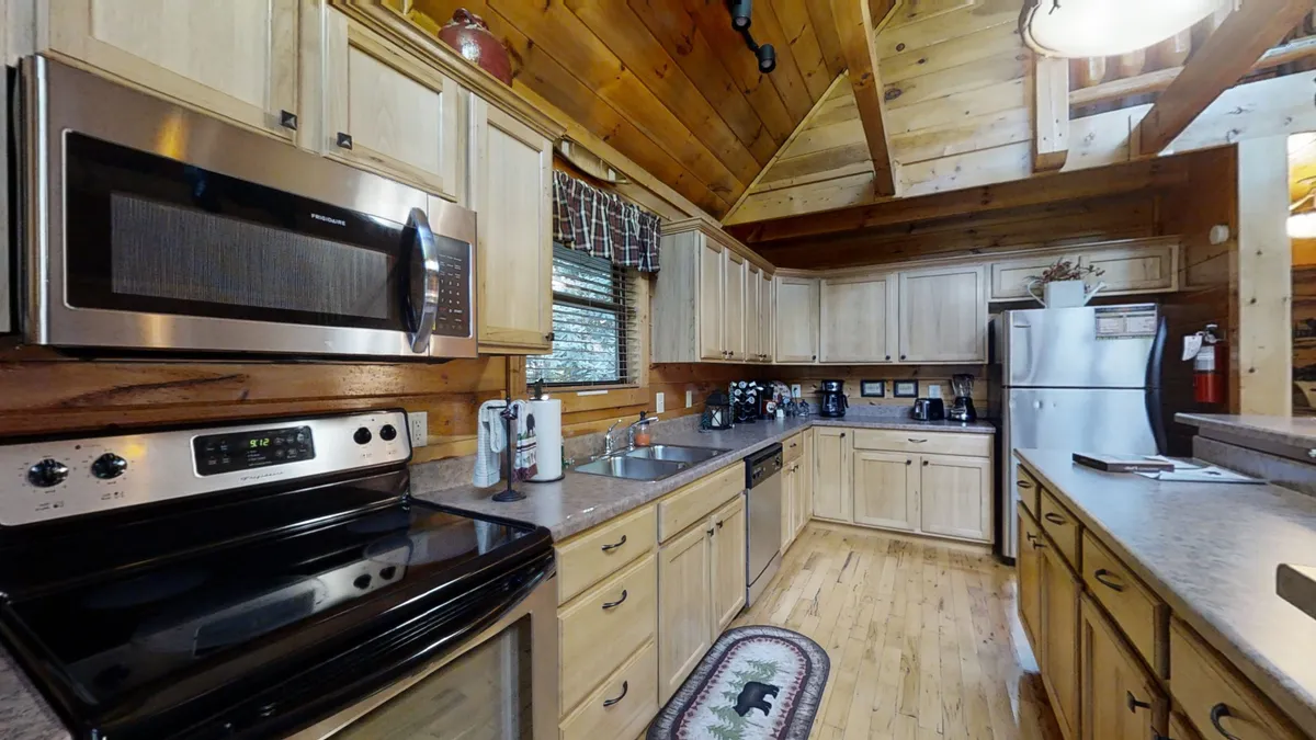 A warm, welcoming kitchen with stainless steel appliances, ample wood cabinetry, a central island, and a rug featuring a bear motif. The kitchen is ready for cooking, gathering, and sharing meals, echoing the themes of togetherness and home-cooked comfort.